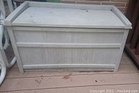 Front view of the SunCast patio storage bench showing textured light tan plastic with panel design and slight dirt marks.