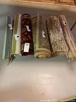 Photo showing six rolled area rugs, varied colors and textures laid side by side on a surface.