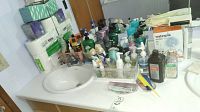 Photo of the bathroom counter with multiple bottles, combs, nail clippers, scissors, and packs of bathroom tissue