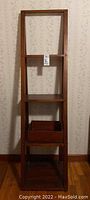 Front view of ladder style wooden shelf with three tiers and wooden storage box on bottom shelf.