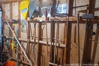 Photo showing various rakes and long-handled tools hung on a wood wall rack.