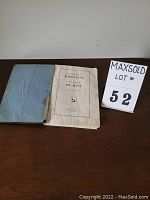 Photo of another view of the book open to title page with visible wear on cover and some loose pages.