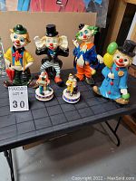 Front view of 4 large clown coin banks and 2 smaller musical clown figurines displayed on black table