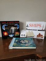 Set of three books shown closed: The Earth Pack with black cover, The Pop-Up Book of Ships with white cover, and If You See a Fairy Ring
