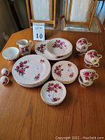 View of the full set showing various sized plates, mugs, small bowl, and pitcher all decorated with pink rose floral motifs and gold edges.