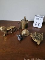 All five brass items on table showing lot contents: lion figurine, benzene can, candle snuffer, countertop bell, sundial compass.