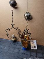 Two vintage hanging light fixtures, one ornate with amber glass panels, the other simpler metal frame with single bulb socket, shown side by side.