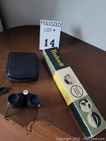 Nikon 9x25 binoculars with black carrying case and Bushnell spotting telescope box on wood table