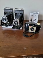 Front and side view of the three vintage cameras grouped on a wooden surface.