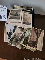 Shoebox full of vintage postcards, mostly black and white scenes with some color cards visible, displayed on a table