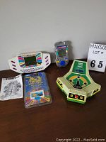 Photo showing four vintage electronic games: Head to Head Baseball game, Wheel of Fortune handheld game with cartridge and instructions, and Rush Hour handheld game.