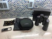 Overview of all four pieces on countertop: two pairs of binoculars, Bose headphones with case, and handheld magnifier with light.