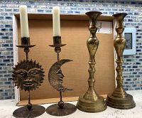 Photo showing all four candle holders together. Two pairs: one artistic hammered metal set including sun and moon face bases, and one brass traditional pair with baluster stems.