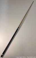 Full view of the pool cue showing one-piece length, light wood shaft with black wrapped handle at the bottom.