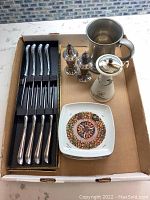 Full box view showing steak cutlery set, salt and pepper shakers, pewter mug, pepper grinder, and a decorative ceramic dish with a spice motif