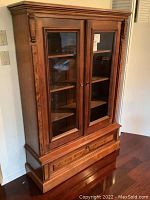 Closed front view of the wooden cabinet with glass-paneled doors and carved details.