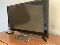 Samsung 32-inch smart TV on wooden surface with remote and user manual in view.