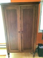 Front view of tall wood cabinet with closed double doors, paneled design and wood finish