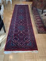 Full length view of red Oriental runner rug unrolled on wood floor