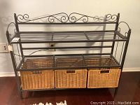 Front view of the wrought iron shelf rack with three wicker baskets inserted on the bottom shelf.