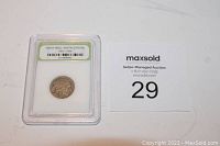 Front photo of the slabbed coin showing the front label with the coin inside and lot number 29 card beside it.