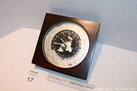 Square desk clock in dark wooden case with aviation-themed world map dial and 24-hour markings, red sweep second hand visible