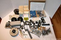 Top-down view of assorted electronics components including digital panel meter experiments kit, analog meters, relays, terminal blocks, and a rheostat box.