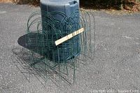 Green garden fencing sections stacked beside a blue container outdoors with a 16 inch ruler for scale, showing the height and shape of the fencing sections.