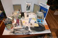 Overall view of the large mixed electronics and accessory lot showing filters, bulbs, tools, and small parts spread on a table.