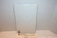 Front view of the white embossed cover comic book showing subtle raised imagery, placed standing inside a clear protective sleeve against a plain backdrop.