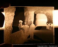 Glass dry plate negative held up to light showing two men and one woman inside a cave.
