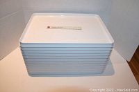 Stack of 12 white rigid plastic serving trays with WestJet logo visible on top tray's upper surface