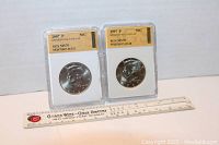 Two slabbed Kennedy Half Dollar coins, dated 2007P and 1997P, with a ruler placed below for scale.