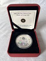 Photo of the 2007 $8 fine silver maple leaf coin in original display box with informational insert visible behind coin.