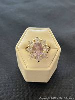 Front view of ring showing oval amethyst-color center stone with eight surrounding clear stones in sterling silver