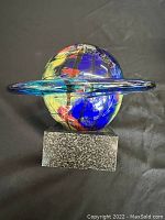 Front view of vintage art glass planet sculpture showing colorful sphere within a blue glass ring on a square stone base