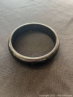 Black jade bangle placed on black textured fabric background, clear view of outer and inner surface showing the dark polished jade material.