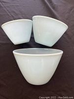 Set of three blue tinted glass Fire King mixing bowls arranged on black fabric, showing exterior shape and size differences.