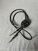 Full length photo of the black leather bolo tie showing the oval clasp and metal tips.