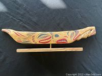 Full side view of the hand-carved wooden canoe mounted on a base, showing painted traditional designs in red, black, and blue.