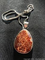 Fire agate pendant and silver chain displayed on black fabric background revealing the polished surface and distinctive internal pattern of the gemstone.