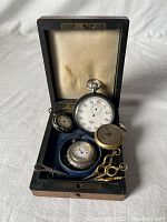 Front view of the lot of five pocket watches and winding keys in an open vintage box.