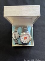 Two vintage wristwatches in a beige box with blue cushion. One shows Marilyn Monroe image, the other has Calgary Flames logo.