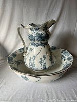 Wash basin with matching pitcher set on white cloth background, showing the blue floral and vine pattern all over both pieces.