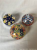 Top view of three Murano millefiori glass paperweights displaying colorful floral cane patterns under smooth glass domes, showing overall shape and color variety.