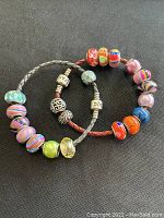 Two Pandora leather bracelets displaying multi-colored glass, crystal, and sterling silver bead charms on a black background.