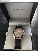 Front view of Perry Ellis wristwatch in box showing dial, chronograph subdials and tachymeter bezel.