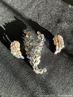 Full lot showing brooch and earrings on black fabric with iridescent stones reflecting light.