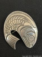 Front view of the salmon-shaped sterling silver pendant/brooch with detailed etched design on a black background.