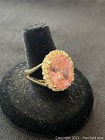 Close-up angled view of sterling silver ring with pink oval faceted gemstone surrounded by halo of small clear stones, displayed on black ring stand.